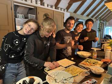 Cinq amis se réunissent dans une cuisine confortable, souriants, et préparent des sushis ensemble. Les ingrédients et les ustensiles sont disposés sur le comptoir, créant une atmosphère joyeuse et collaborative.