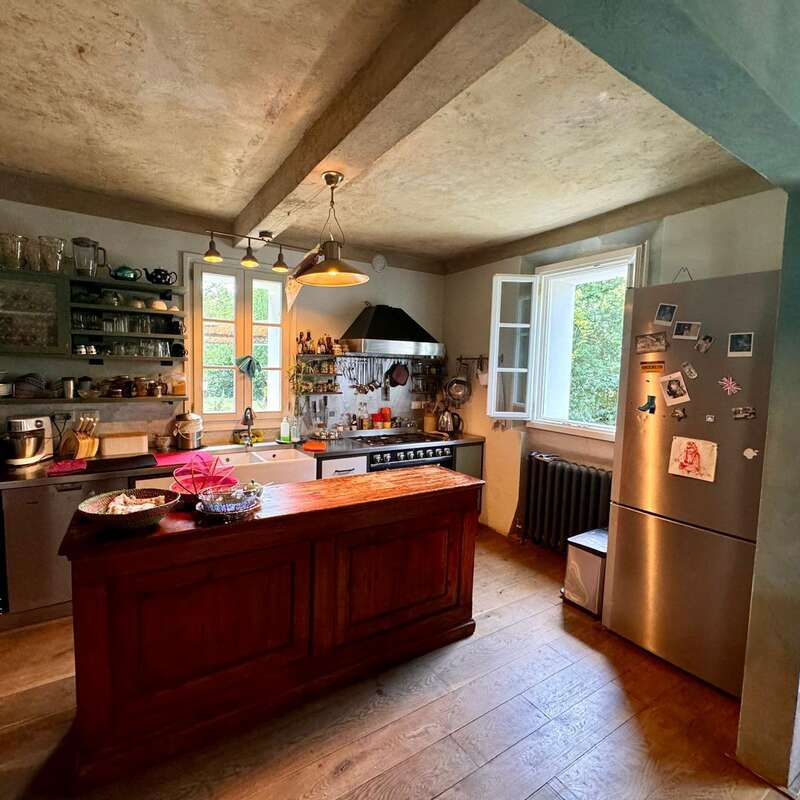 Esta cocina destaca por su encanto rústico, con una isla de madera, estantes abiertos, utensilios colgados, un fregadero de estilo rústico, una nevera de acero inoxidable, una ventana abierta, luz natural y un ambiente acogedor y hogareño.