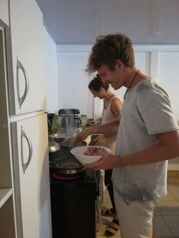 The image depicts a man and woman cooking in a kitchen, with the man holding a bowl of food and the woman standing beside him at a stove.
