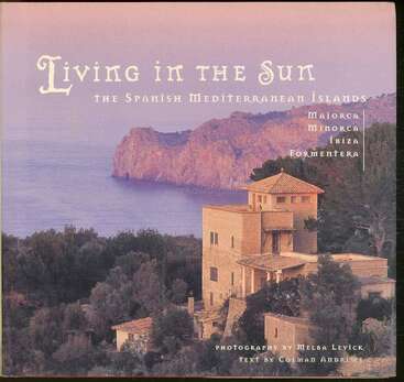 Dieses Bild zeigt ein Buchcover mit dem Titel "Living in the Sun: Die spanischen Mittelmeerinseln". Es zeigt eine mediterrane Villa, Küstenklippen, üppiges Grün und ruhiges Wasser.