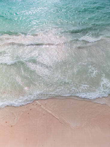 Sanfte türkisfarbene Wellen rollen an einen weichen Sandstrand. Das Sonnenlicht funkelt auf dem Wasser und schafft eine friedliche, tropische und einladende Küste mit ruhiger Atmosphäre.