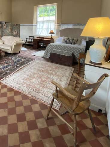 La imagen muestra una acogedora habitación con cama, sofá y alfombra, suelo a cuadros y una ventana con vistas a los árboles del exterior, que desprende un ambiente cálido y acogedor.