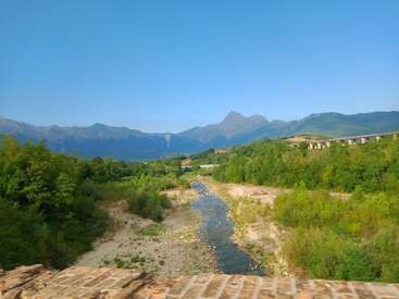 The image depicts a serene landscape featuring a river, lush greenery, and distant mountains, with a bridge visible on the right side of the scene.