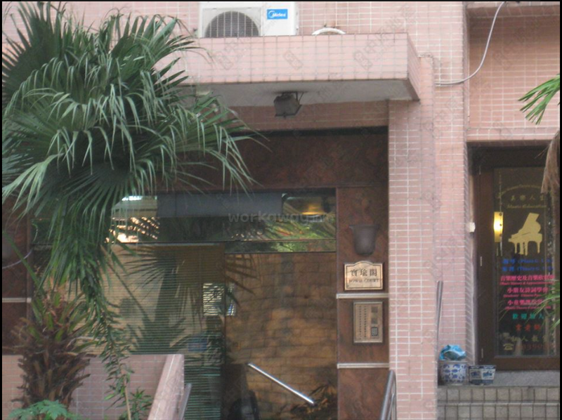L'image représente l'entrée d'un bâtiment avec une porte en verre, comportant un palmier et une enseigne avec des caractères chinois, entourée d'une façade en briques.