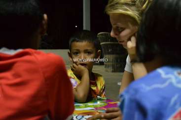 The image depicts a woman and three children gathered around a table, with the woman and one child in the foreground and two children in the background.