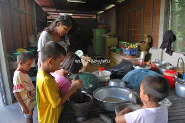 The image depicts a group of children and an adult in a kitchen, surrounded by various cooking utensils and ingredients. The scene appears to be a cooking class or activity.