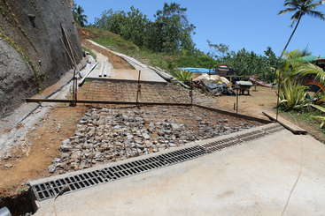 Das Bild zeigt eine Baustelle mit einem Betonfundament, einem Metallrahmen und einer Holzkonstruktion, wahrscheinlich für ein Gebäude oder eine Brücke, mit einem Metallgeländer und einem Betonsockel.