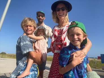 Una feliz familia de cinco miembros posa al aire libre en un día soleado. Los padres y los tres hijos sonríen, llevan ropa informal de verano y sombreros. Fondo de cielo azul.