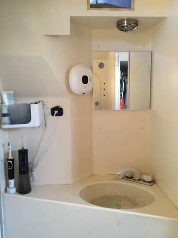 This is a small, minimalist bathroom with a round sink, wall-mounted mirror, soap dispenser, electric toothbrush, water flosser, shelf, and overhead light fixture.