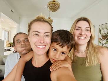 Cuatro personas posan para una alegre selfie en el interior, con una cálida sonrisa. Una de ellas pone una mueca graciosa, mientras un niño pequeño abraza a la mujer del centro. El ambiente es muy alegre.