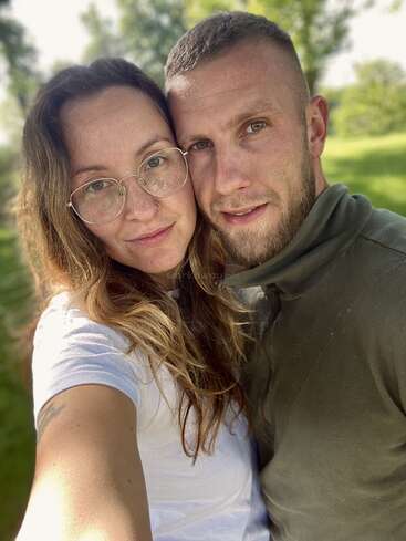Das Bild zeigt ein Selfie von einem Mann und einer Frau, die sich umarmen. Die Frau steht links und der Mann rechts, beide haben helle Haut und lange Haare.