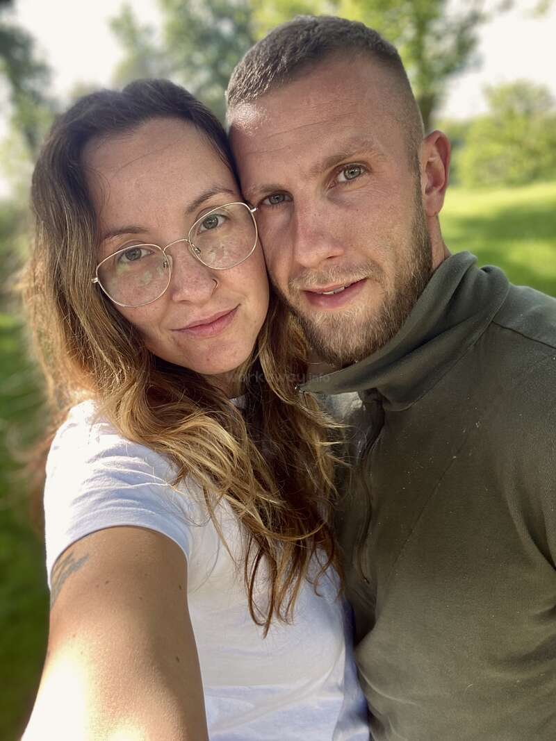 Das Bild zeigt ein Selfie von einem Mann und einer Frau, die sich umarmen. Die Frau steht links und der Mann rechts, beide haben helle Haut und lange Haare.