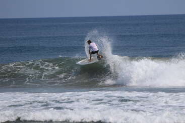 A surfer rides a breaking wave, skillfully maneuvering his board along the crest. Ocean water splashes high, capturing the thrill and energy of surfing perfectly.