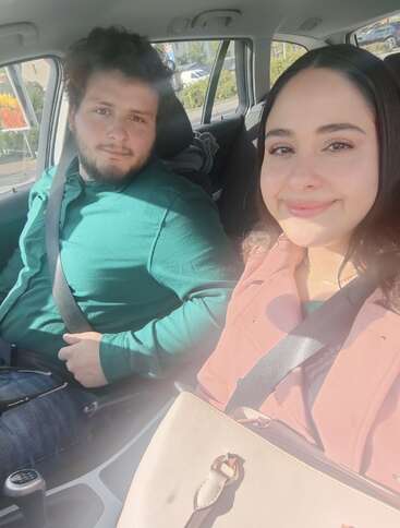 Un hombre y una mujer están sentados en un coche, ambos con el cinturón de seguridad puesto. Sonríen, disfrutan de un día soleado y parecen felices juntos.
