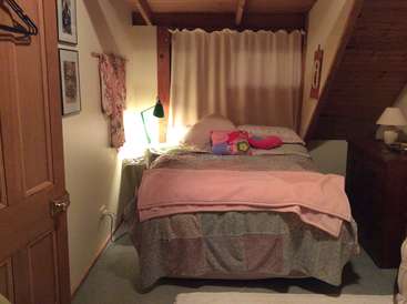 La imagen representa un acogedor dormitorio con cama, mesilla de noche y lámpara, que ofrece un ambiente cálido y acogedor con una mezcla de tonos de madera y una iluminación suave.