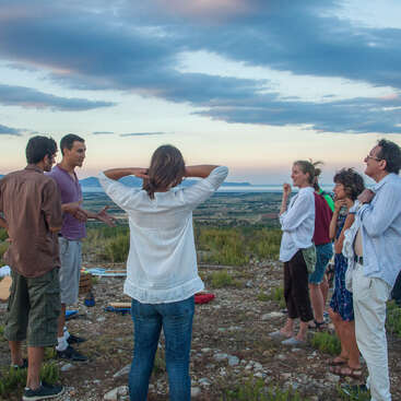 The image depicts a group of people standing on a rocky hilltop, gazing out at a vast landscape, with a cloudy sky above them.