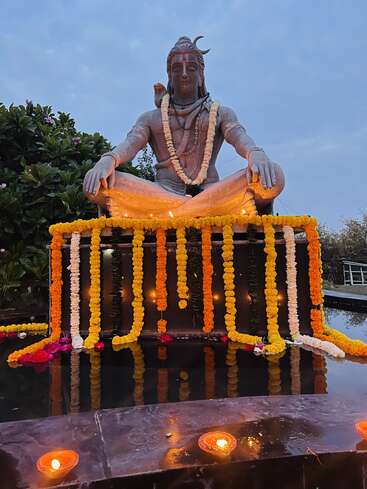 Eine wunderschön geschmückte Lord Shiva-Statue sitzt in Meditation. Umgeben von Ringelblumengirlanden, Öllampen, Blumen und Wasser schafft sie eine ruhige und spirituelle Atmosphäre.