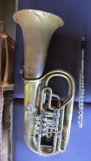 This image shows a large brass wind instrument next to a smaller silver flute, both resting on a dark surface, contrasting in size and type.