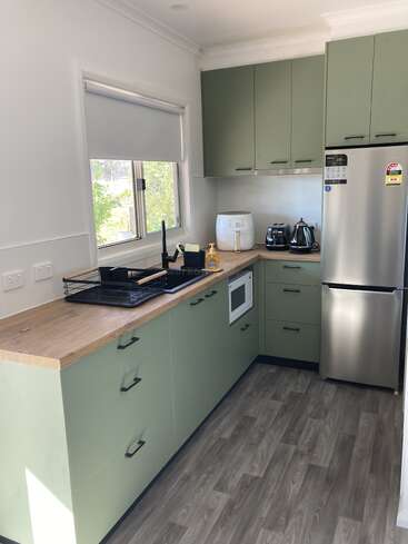 This kitchen features sage green cabinets, wooden countertops, and modern appliances, including a fridge, toaster, kettle, and air fryer. There's a window providing natural light.