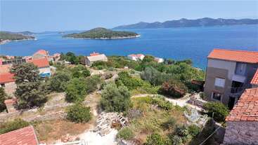 This image shows a scenic coastal village with red-roofed houses, lush greenery, and a beautiful blue sea surrounded by small islands and distant mountains. Peaceful atmosphere.