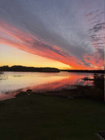 A stunning sunset over a calm lake, vibrant orange and pink clouds stretch across the sky, reflecting beautifully on the tranquil water. Peaceful nature scene.