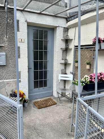 Cette entrée extérieure chaleureuse est agrémentée d'une porte bleu-gris, d'une petite table avec une chaise, de pots de fleurs colorés, d'un paillasson et d'étagères sur lesquelles sont disposés de petits bocaux en verre.