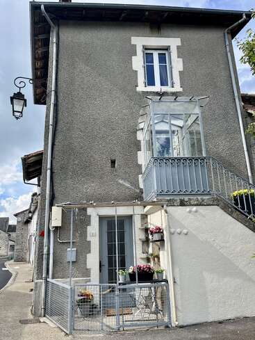 Cette photo montre une charmante petite maison en pierre aux murs gris et aux moulures blanches, agrémentée de fleurs en pot, de grilles en fer forgé et d'un lampadaire classique.