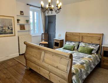 Cette chambre confortable est équipée d'un lit en bois avec une literie aux motifs tropicaux, d'un lustre, de tables de chevet, d'une fenêtre avec des rideaux, d'étagères décorées, d'œuvres d'art et d'un parquet.