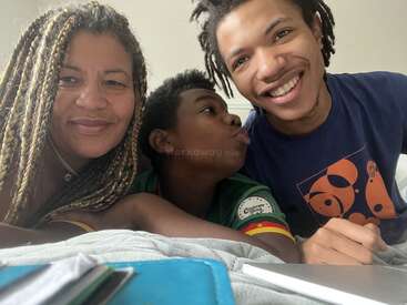 A woman and two boys are laying on a bed, smiling warmly at the camera. They appear happy and relaxed, capturing a joyful, candid family moment together.