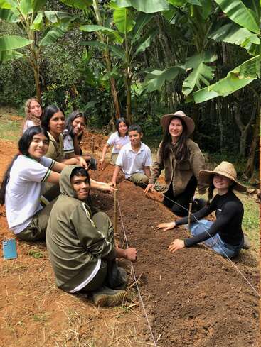 A group of young people happily planting seeds in a garden bed, surrounded by lush banana trees, working together outdoors in nature, smiling and enjoying teamwork.