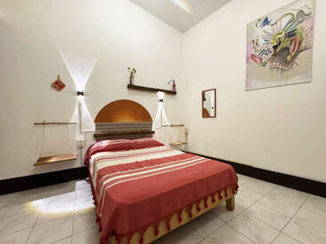 Cette photo montre une chambre à coucher chaleureuse avec un couvre-lit rouge, des étagères murales suspendues, une décoration minimaliste, des murs blancs, des œuvres d'art, un miroir et un éclairage tamisé.
