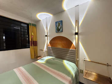 Une chambre chaleureuse avec des motifs lumineux originaux sur les murs, un tableau représentant un cactus au-dessus du lit, des rideaux jaunes, des tables de chevet suspendues et un couvre-lit à rayures vertes.