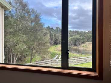 A window view shows a lush green landscape, trees, a wooden fence, and a small pond under a cloudy sky, creating a peaceful rural scene.