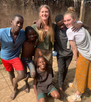 The image shows a group of five people, including two women and three children, posing for a photo together outdoors on a sunny day.