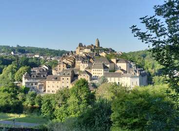 A picturesque hillside village with charming stone houses and a prominent church steeple, surrounded by lush greenery under a clear blue sky, exuding peaceful countryside charm.