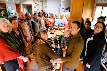 Un groupe de personnes se tient en cercle autour d'une grande table à manger, se tenant par la main, souriant, fêtant ensemble dans un cadre chaleureux et douillet de cuisine familiale.