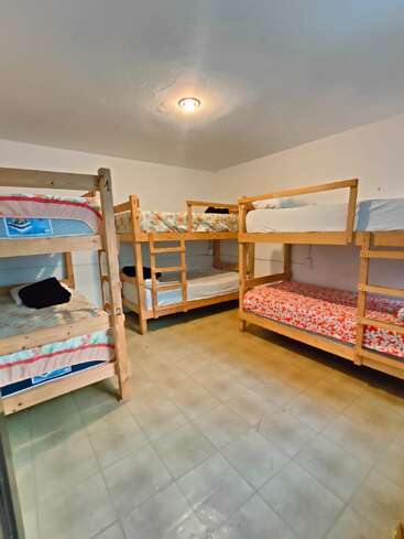 Cette photo montre une chambre propre et sobre, équipée de quatre lits superposés en bois, chacun recouvert d'une literie colorée. Le sol est carrelé et la pièce est bien éclairée.