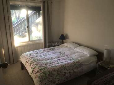 The image depicts a serene bedroom with a large window, featuring a bed adorned with a floral comforter, a nightstand, and a lamp, bathed in natural light.