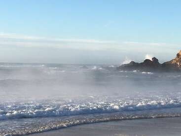 The image depicts a serene beach scene with waves gently lapping at the shore, set against a backdrop of a clear blue sky and distant rocky outcroppings.