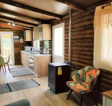 L'intérieur chaleureux de ce chalet en rondins se caractérise par une cuisine moderne, un fauteuil à motifs, un poêle à bois, des murs en bois, un coin repas, une belle lumière naturelle et une ambiance épurée et accueillante.