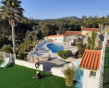 Cette photo montre une magnifique villa avec piscine, nichée au cœur d'un écrin de verdure et d'arbres. Deux personnes se détendent sur du gazon synthétique, profitant du calme de cet espace extérieur.