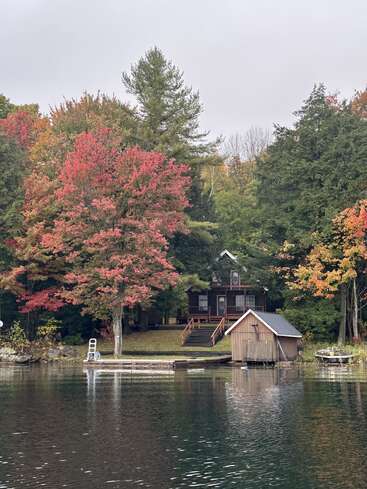 Une cabane confortable se trouve au bord d'un lac calme entouré d'arbres d'automne colorés. Un quai en bois et un hangar à bateaux complètent cette paisible et pittoresque scène d'automne au bord d'un lac.
