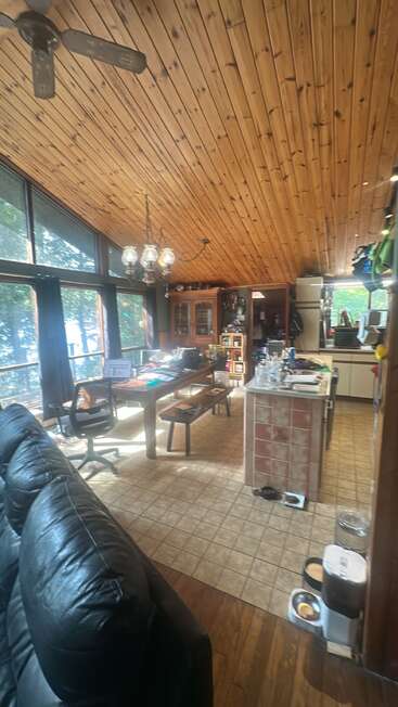 Die gemütliche, sonnendurchflutete Hütte verfügt über eine schräge Holzdecke, große Fenster, eine Küchenzeile, einen Esstisch, ein schwarzes Sofa, Fliesenböden und Futternäpfe für Haustiere.
