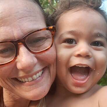 A joyful close-up selfie of an older woman wearing glasses and a young child. Both are smiling widely, radiating happiness and capturing a playful, loving moment.
