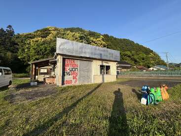 A small, weathered building stands on grassy land, featuring graffiti that reads "INTER-NATION IF WON CENSOR BE LOUD" with colorful animal sculptures and long shadows nearby.