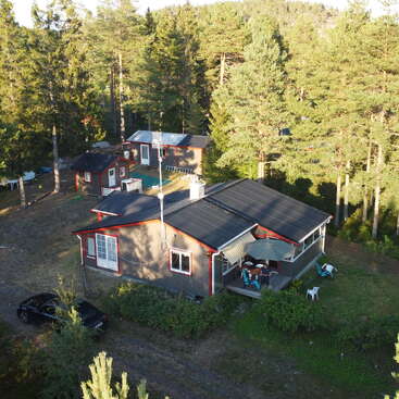 A imagem retrata uma área residencial serena com várias casas, cercada por árvores, com um carro, móveis de pátio e vegetação exuberante, capturada de uma perspectiva aérea.