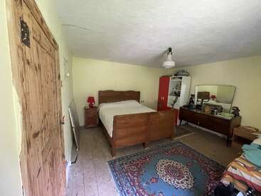 This bedroom features a wooden bed, vintage furniture, a large decorative rug, a cupboard, a dresser with a mirror, soft yellow walls, and simple decor.