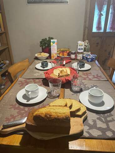 A cozy breakfast table is set with cups, glasses, pound cake, juice, fruit, yogurt, and condiments, creating a warm and inviting atmosphere for four people.