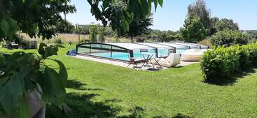 Ein ruhiger Garten mit sattgrünem Rasen, einem überdachten Pool, Sitzgelegenheiten im Freien, Sitzsäcken und Bäumen im strahlenden Sonnenlicht – ein Ort der Ruhe und Entspannung.