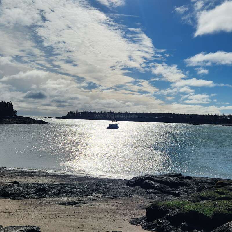 Una serena escena costera con un barco flotando en aguas centelleantes. El cielo está parcialmente nublado, la luz del sol se refleja maravillosamente, mientras que las costas rocosas y los árboles distantes enmarcan la vista.